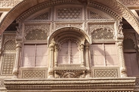 Intricate stone carvings adorn a facade rich with lattice work and detailed ornamentation, highlighting traditional architectural craftsmanship. The structure features geometric patterns and arched designs, suggestive of historical and cultural significance.