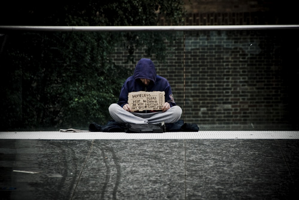 man in blue hoodie reading book on gray concrete road during daytime