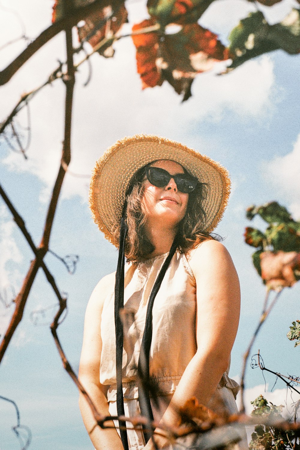 woman in white tank top wearing brown sun hat standing near bare tree during daytime