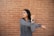 A person is stretching their arm across their chest, wearing a gray jacket and a smartwatch. The background consists of a textured brick wall, creating a casual urban setting.