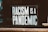 A sign with bold, white text reading 'RACISM IS A PANDEMIC' placed against a dark background. The lettering is highly visible and occupies most of the image. A small part of a book is visible in the bottom right corner.