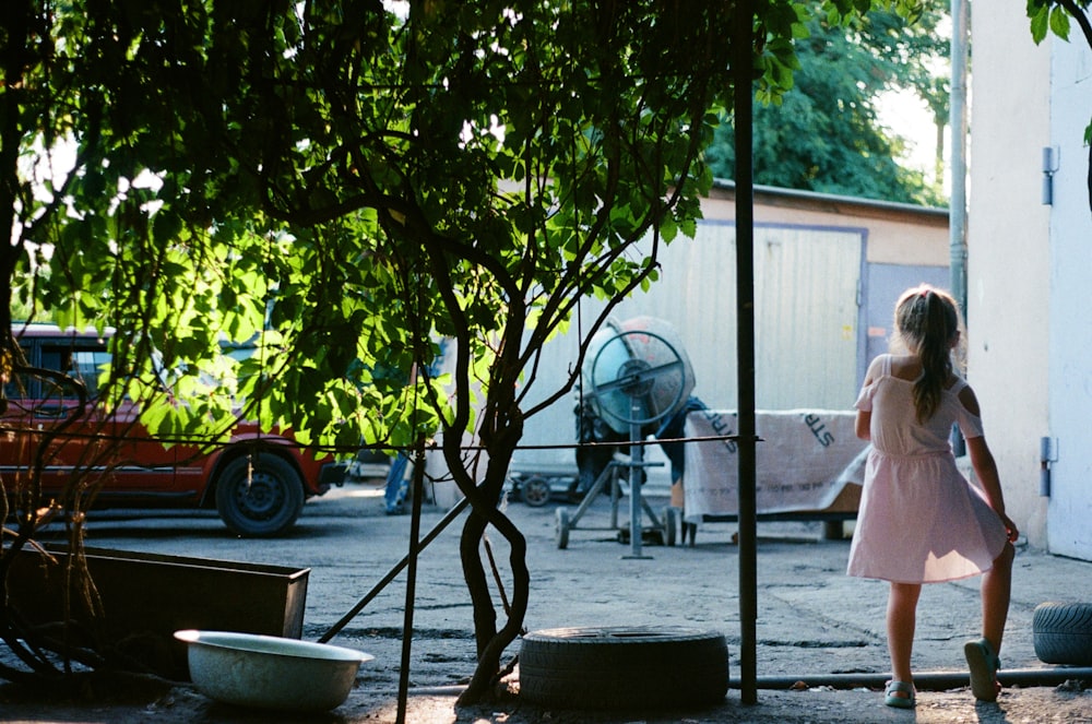 Femme en robe blanche debout près de l’arbre vert pendant la journée