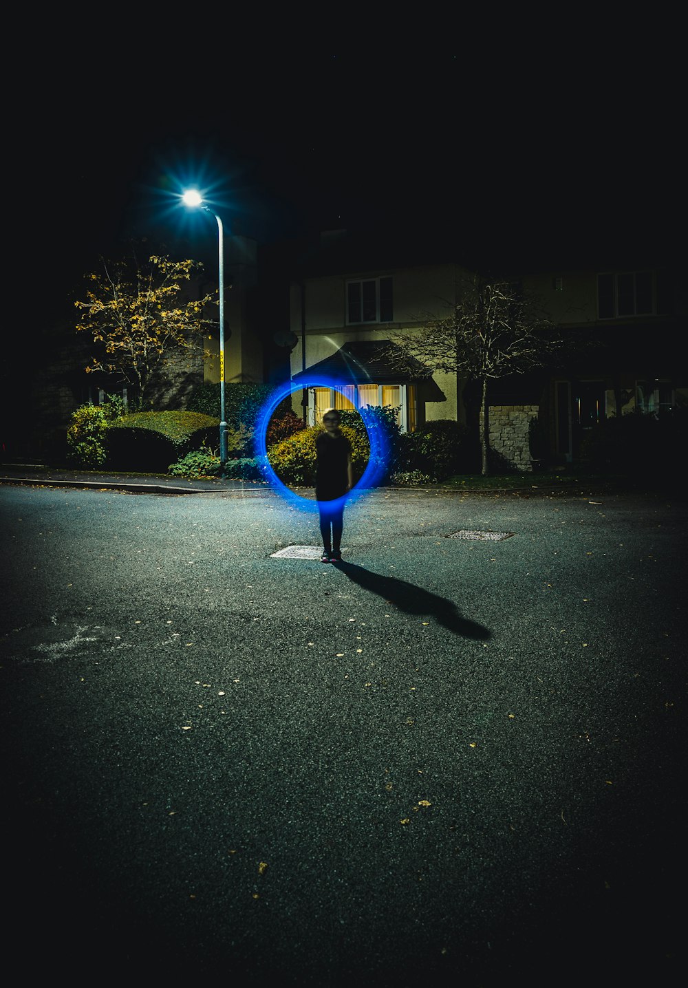 Persona sosteniendo una pelota redonda azul en una carretera de asfalto gris durante la noche