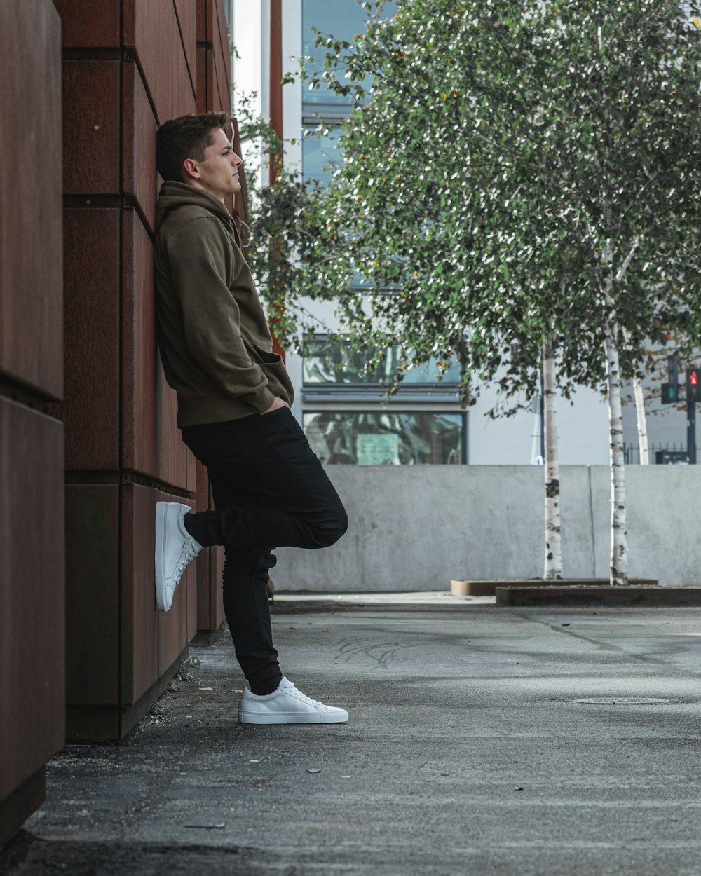 man in brown jacket and black pants standing on sidewalk during daytime