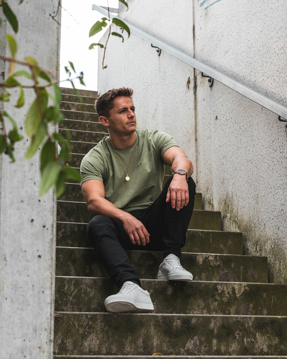 man in green polo shirt and black pants sitting on gray concrete stairs