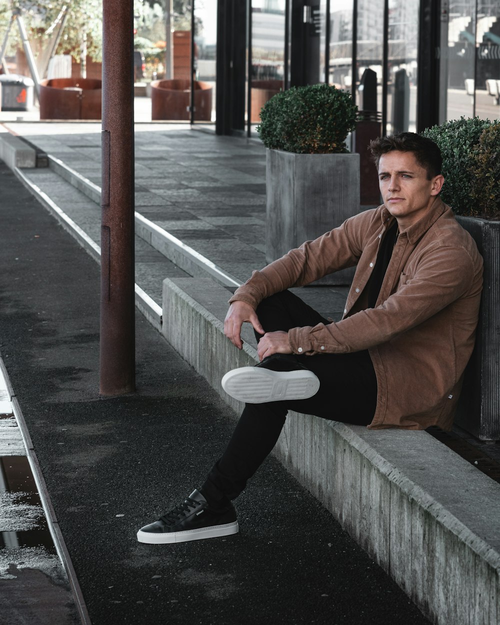 man in brown jacket sitting on sidewalk during daytime