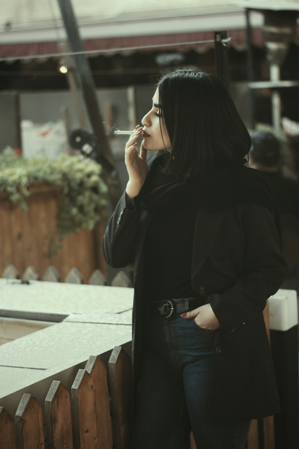 woman in black coat standing near brown wooden fence during daytime