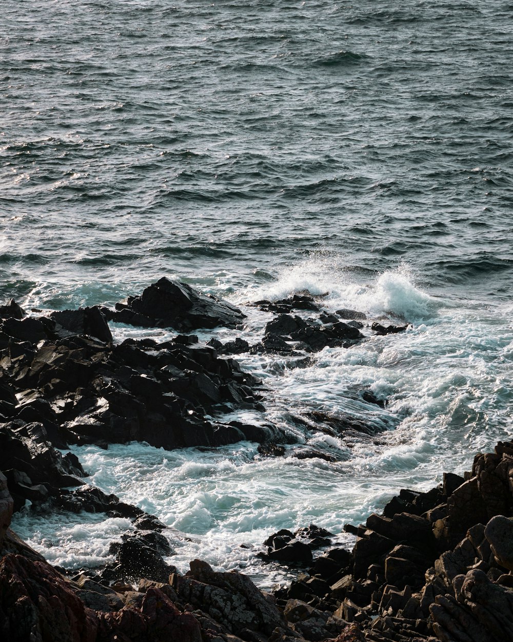 black rocky shore with ocean waves crashing on rocks during daytime