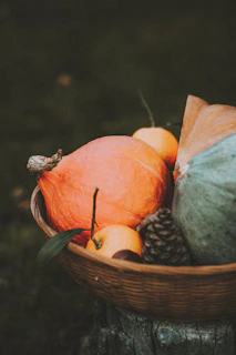 A charming basket overflowing with colorful gourds and autumn leaves resting beside a wooden bench.