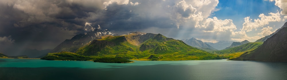 Montagnes verdoyantes près du plan d’eau sous un ciel nuageux pendant la journée