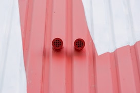 Two small, red circular vents are attached to a red and white corrugated metal surface.