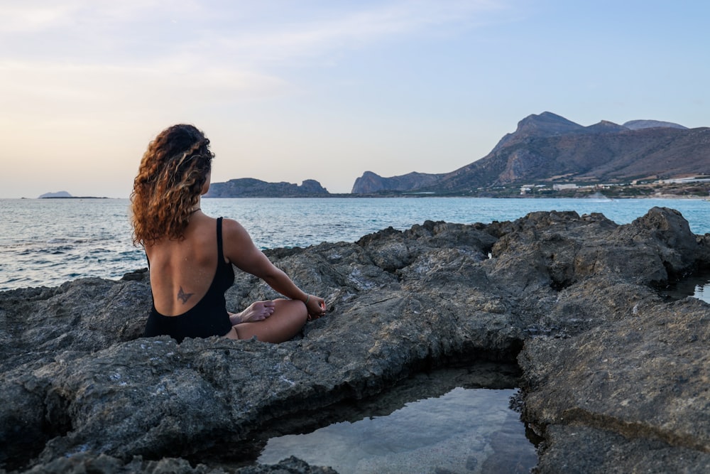 woman in black bikini sitting on rock formation near sea during daytime