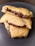 A stack of homemade cookies filled with melted chocolate is placed on a dark plate. The cookies have a golden-brown crust, and the melted chocolate is visibly oozing out from the center, creating a tempting and delicious appearance.