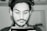 A monochrome portrait of a person with wavy dark hair and a trimmed beard, focused on the screen of a smartphone held in their hands. The lighting emphasizes facial features and creates a soft contrast.