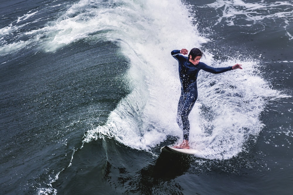 昼間に海の波でサーフィンをする黒いウェットスーツの男