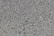 A close-up view of a rough asphalt surface composed of small, uneven gravel and stone pieces. The texture is coarse and heterogeneous, with various shades of gray and occasional hints of brown.