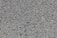 A close-up view of a rough asphalt surface composed of small, uneven gravel and stone pieces. The texture is coarse and heterogeneous, with various shades of gray and occasional hints of brown.
