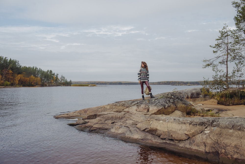 man in red and white plaid shirt standing on brown rock near body of water during