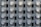 A grid of electric meters is mounted on a grey panel, arranged in neat, aligned rows and columns. Each meter has a circular, glass-covered display with numerical readouts and labels, encased in a metallic frame.