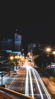 A wide shot of a bustling city street at night, captured with long exposure to highlight light trails.
