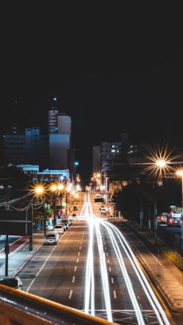 A wide shot of a bustling city street at night, captured with long exposure to highlight light trails.