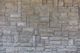 A textured, interlocking pattern of rectangular stone bricks in varying shades of beige and gray, creating a rustic and sturdy appearance.