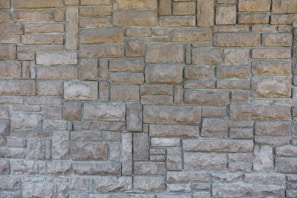 A textured, interlocking pattern of rectangular stone bricks in varying shades of beige and gray, creating a rustic and sturdy appearance.