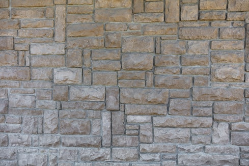 A textured, interlocking pattern of rectangular stone bricks in varying shades of beige and gray, creating a rustic and sturdy appearance.