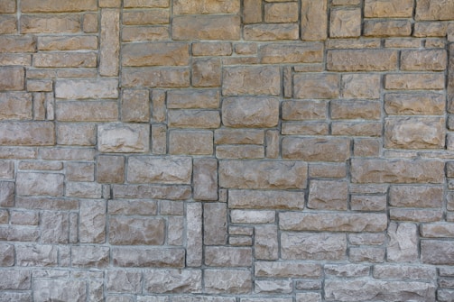 A textured, interlocking pattern of rectangular stone bricks in varying shades of beige and gray, creating a rustic and sturdy appearance.