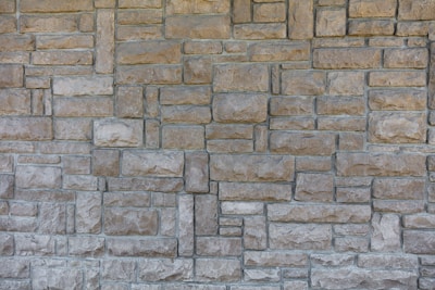 A textured, interlocking pattern of rectangular stone bricks in varying shades of beige and gray, creating a rustic and sturdy appearance.