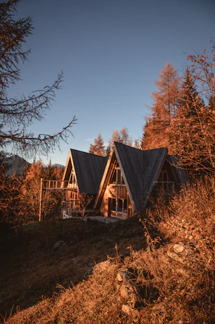 A cozy mountain cabin surrounded by autumn trees under a golden sunset.