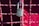 A metallic padlock with a keyhole marked 'BEST' hangs on a grid of metallic wires painted in a reddish hue. The background features a blurred red surface providing a vibrant contrast to the lock.
