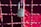 A metallic padlock with a keyhole marked 'BEST' hangs on a grid of metallic wires painted in a reddish hue. The background features a blurred red surface providing a vibrant contrast to the lock.