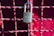 A metallic padlock with a keyhole marked 'BEST' hangs on a grid of metallic wires painted in a reddish hue. The background features a blurred red surface providing a vibrant contrast to the lock.