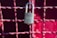 A metallic padlock with a keyhole marked 'BEST' hangs on a grid of metallic wires painted in a reddish hue. The background features a blurred red surface providing a vibrant contrast to the lock.