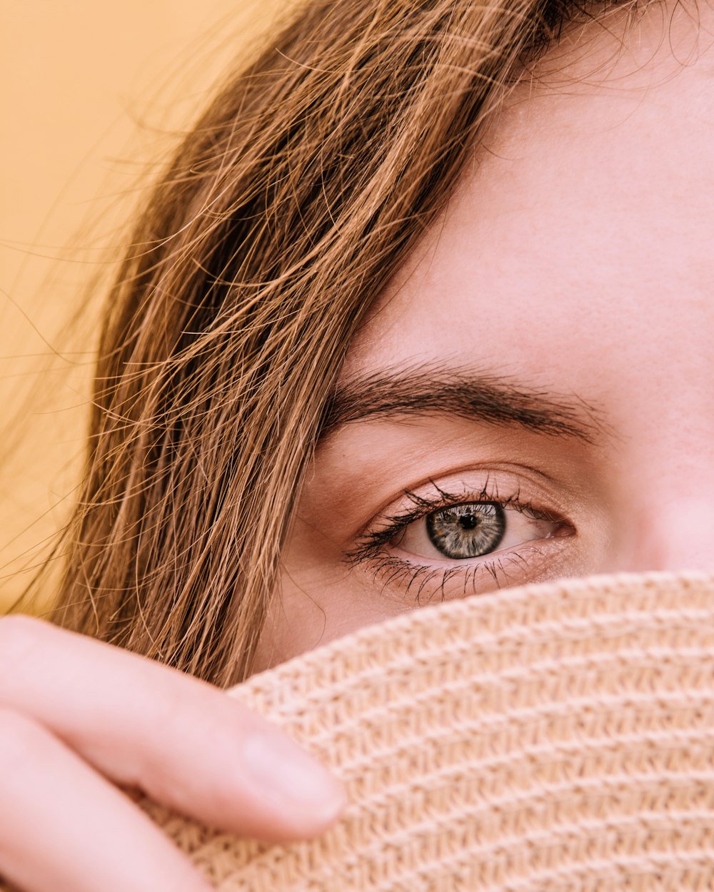 woman covering her face with beige knit textile
