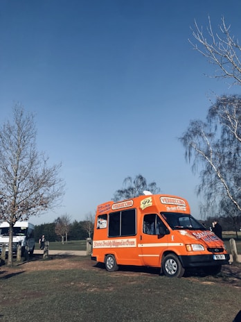 A bright blue-and-white ice cream van parked on a sunny Essex street with happy families gathered around.
