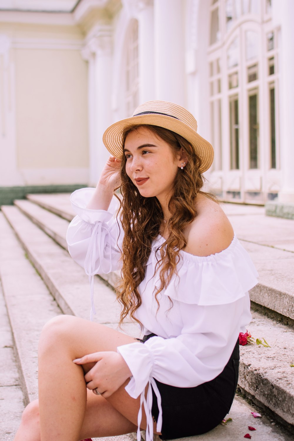 woman in white off shoulder dress wearing brown hat sitting on concrete floor during daytime