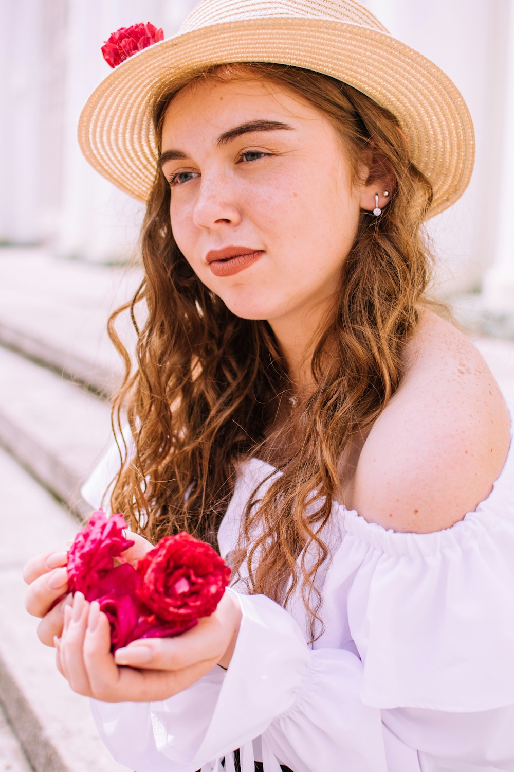 woman in white off shoulder shirt wearing brown straw hat holding red flower