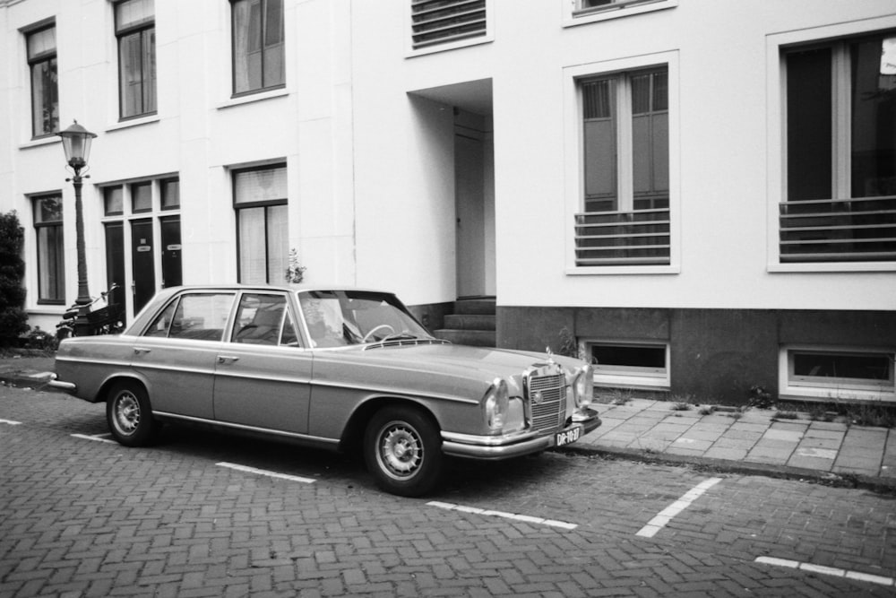 grayscale photo of classic car parked beside building