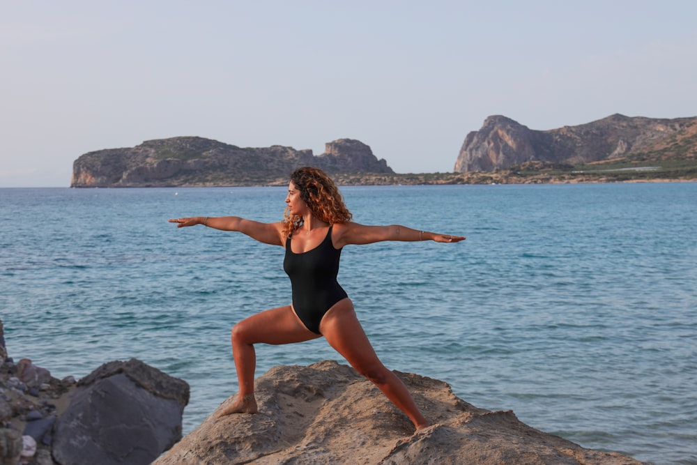 woman in black swimsuit standing on rock near body of water during daytime