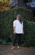 woman in white button up shirt and black pants standing near green plants during daytime