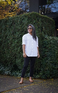 woman in white button up shirt and black pants standing near green plants during daytime