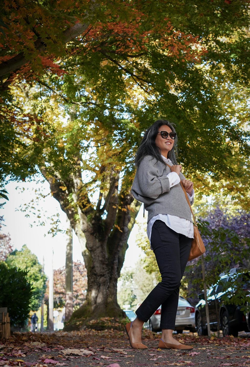 woman in gray long sleeve shirt and black pants standing under green tree during daytime