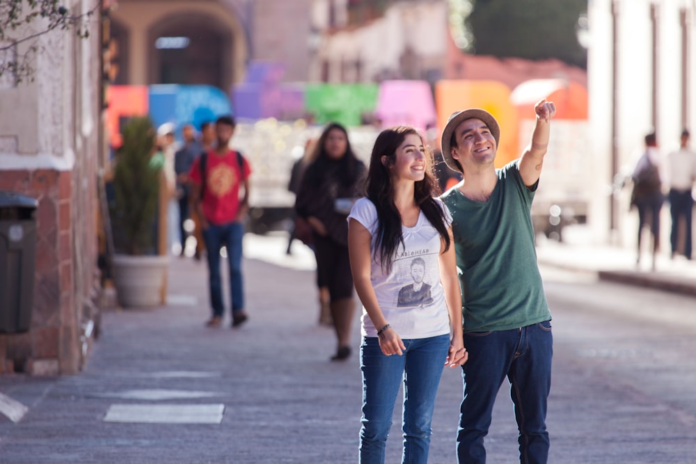 man in green crew neck t-shirt and blue denim jeans standing beside woman in black