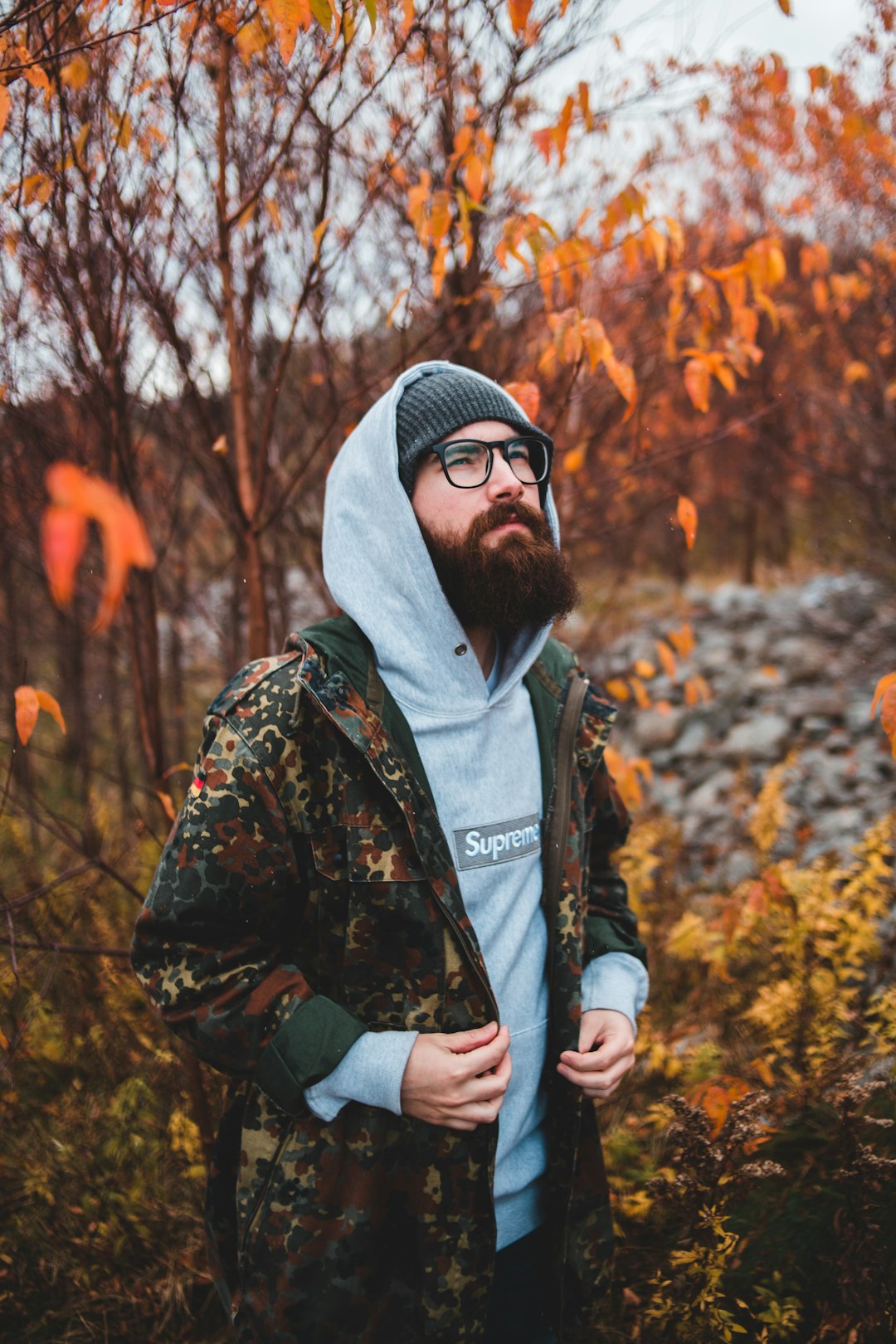 man in black and brown camouflage hoodie wearing gray knit cap standing near brown trees during