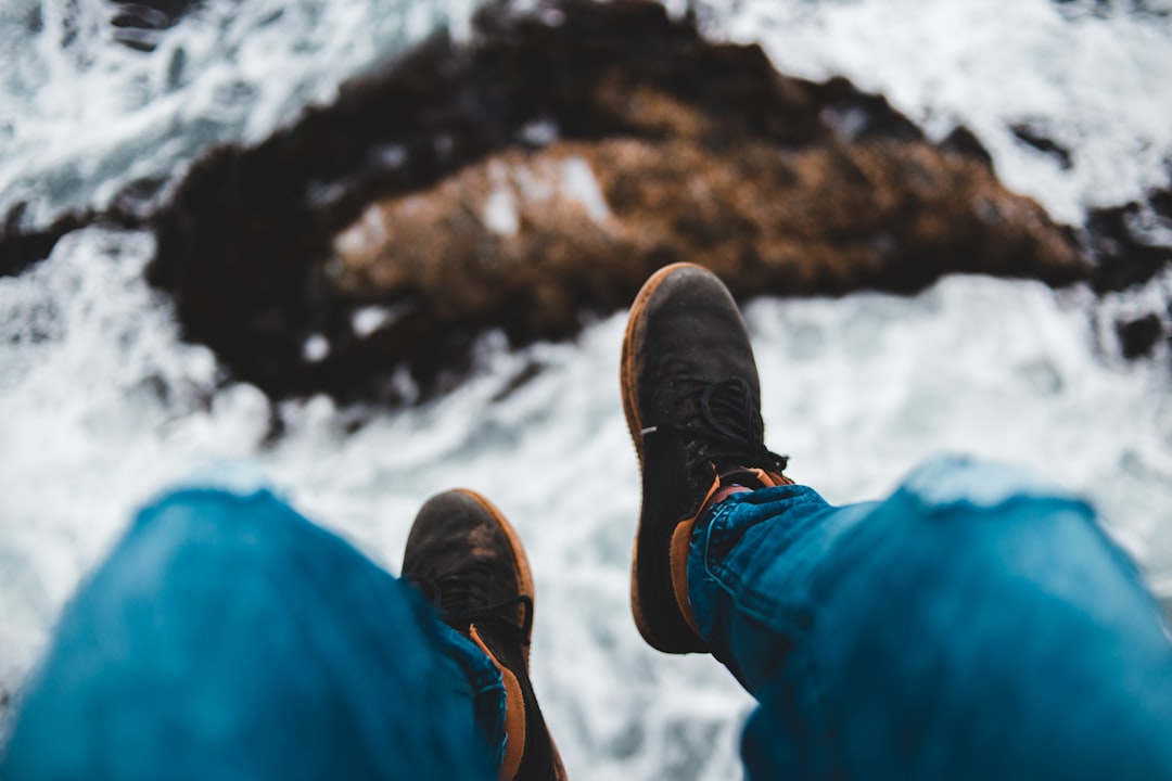 person in blue denim jeans and brown shoes sitting on rock during daytime