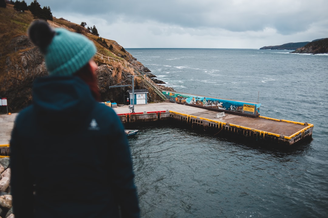 man in black jacket and blue knit cap standing on brown wooden dock during daytime