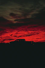 A powerful semi-truck silhouetted against a deep orange sunset on an open highway.