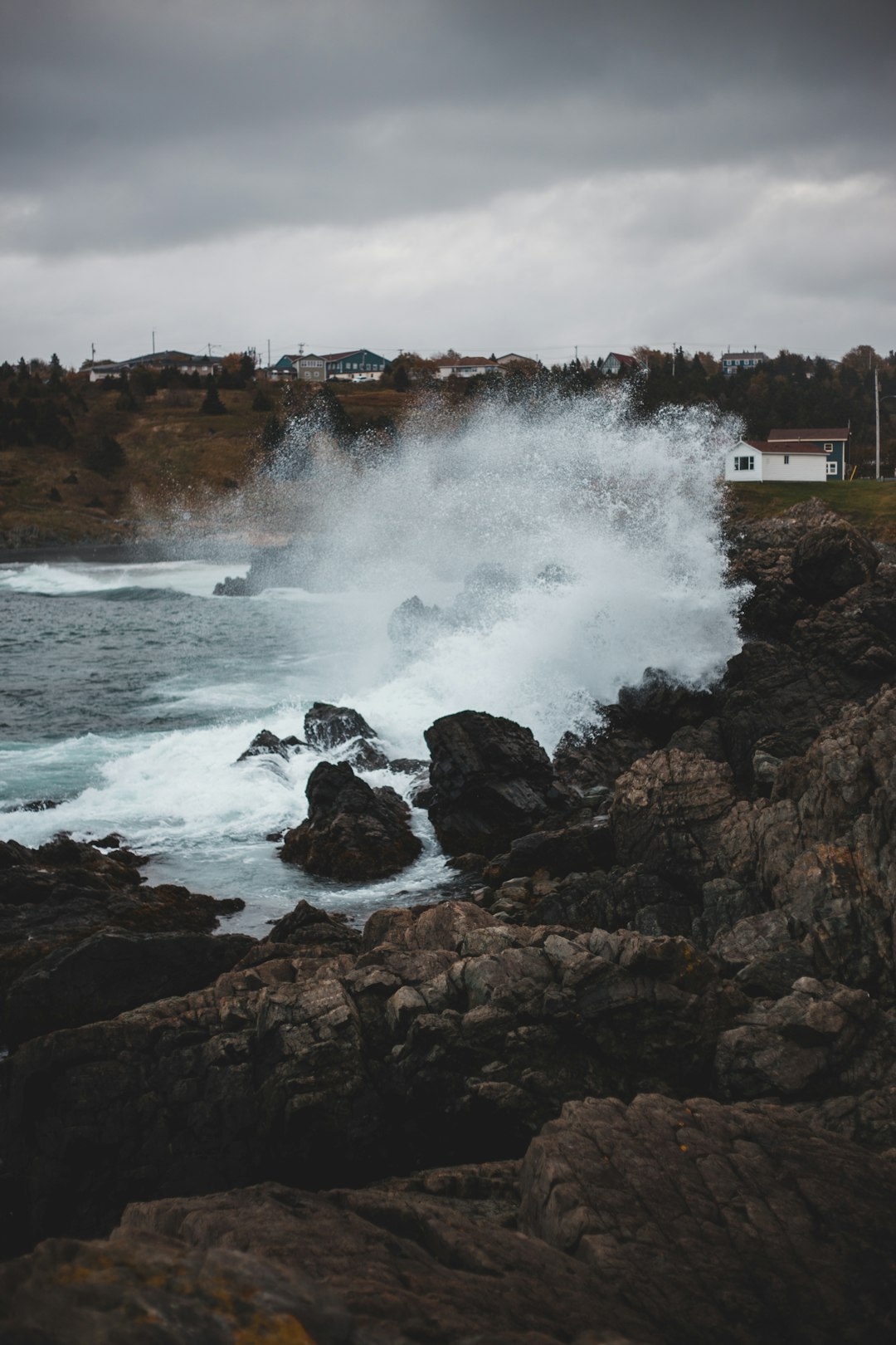 white and brown house on brown rock formation near sea waves crashing on shore during daytime